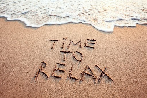 The words “Time to relax” written in sand, symbolizing relaxation and stress relief.